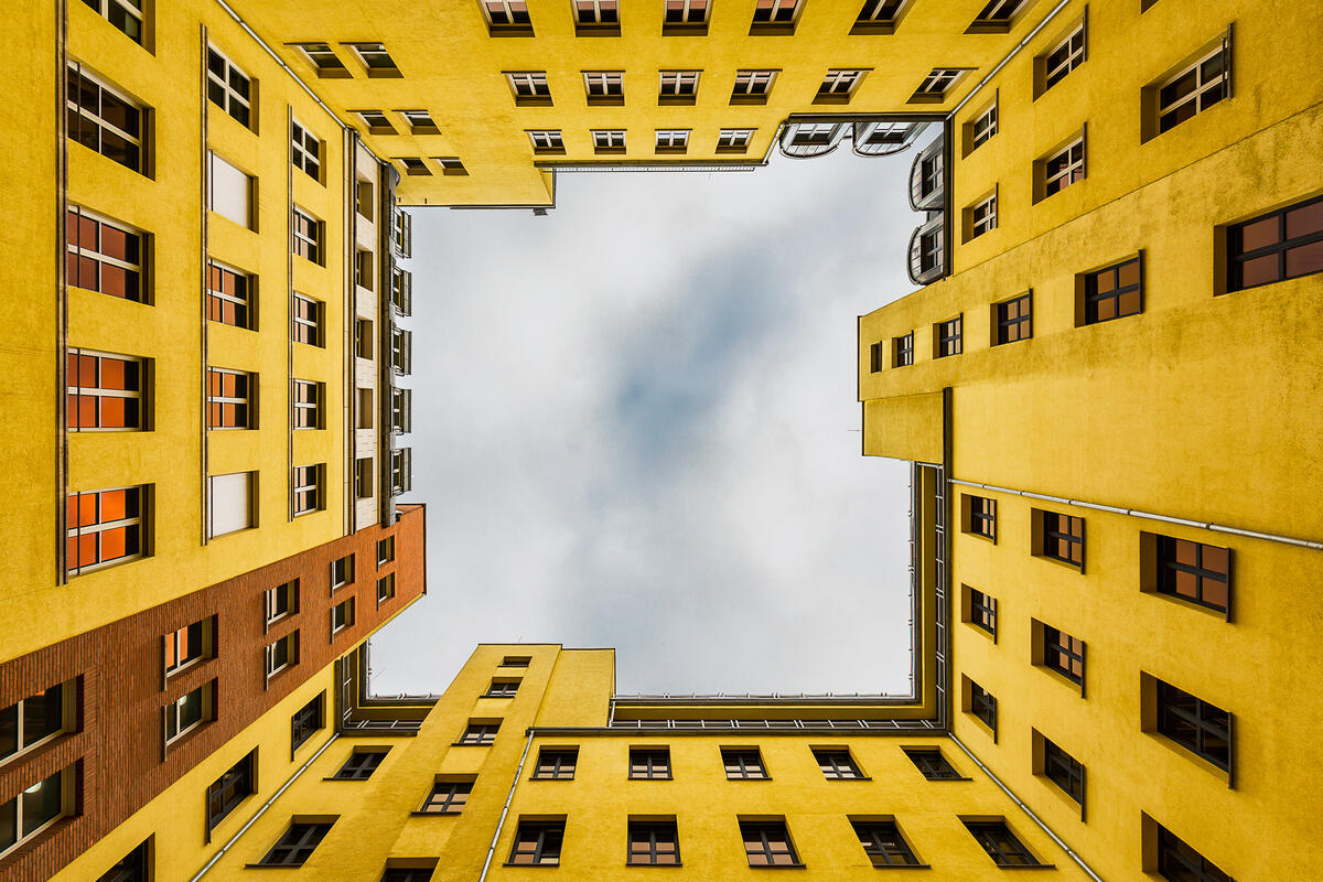 Looking up from a courtyard in Quartier Schützenstraße, where yellow facades frame the cloudy sky.