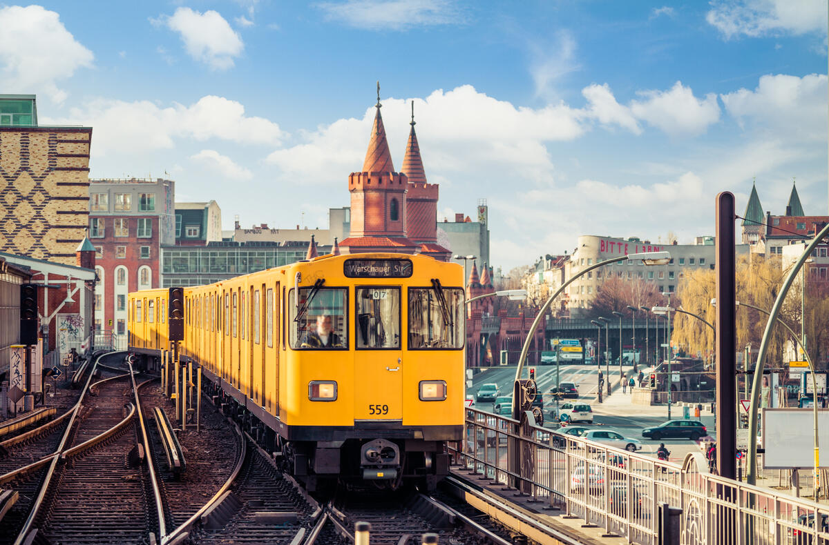 A yellow U-Bahn train passes the red towers of Oberbaum Bridge beneath bright clouds.