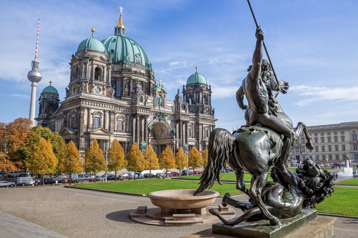 Berlin Cathedral and the TV Tower behind a bronze equestrian statue and trees in autumn colours.