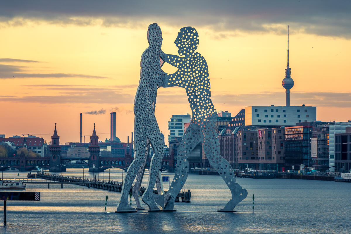 The Molecule Man sculpture in the Spree against a golden sky, with Oberbaum Bridge and the TV Tower behind.