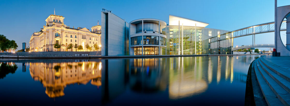 The Reichstag and Paul-Löbe-Haus by the Spree, with illuminated facades and reflections at blue hour.