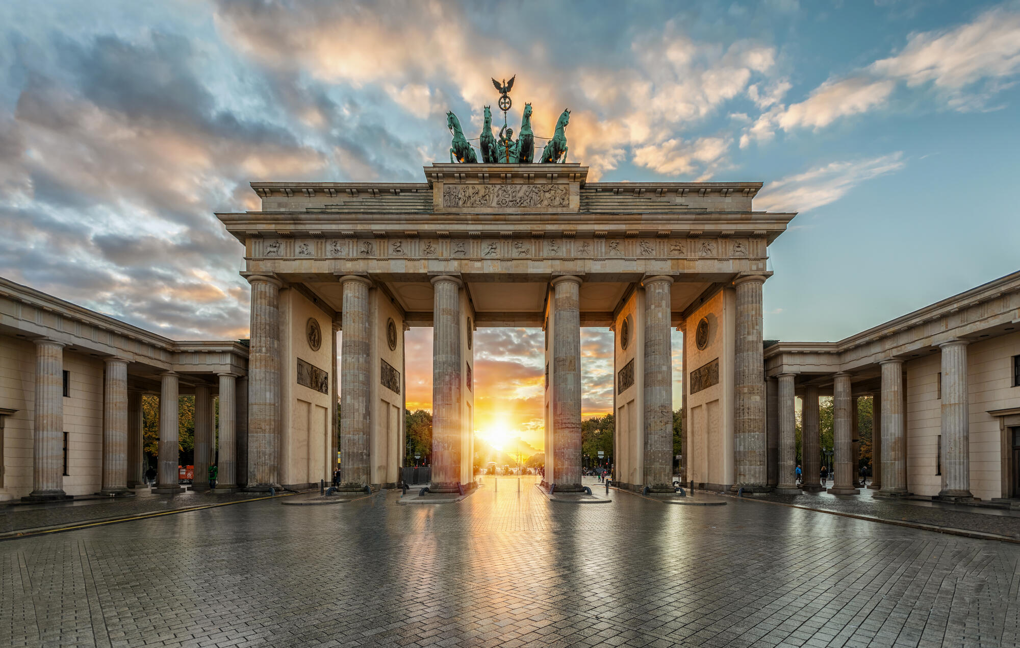 The low sun shines through Brandenburg Gate beneath a cloudy sky.