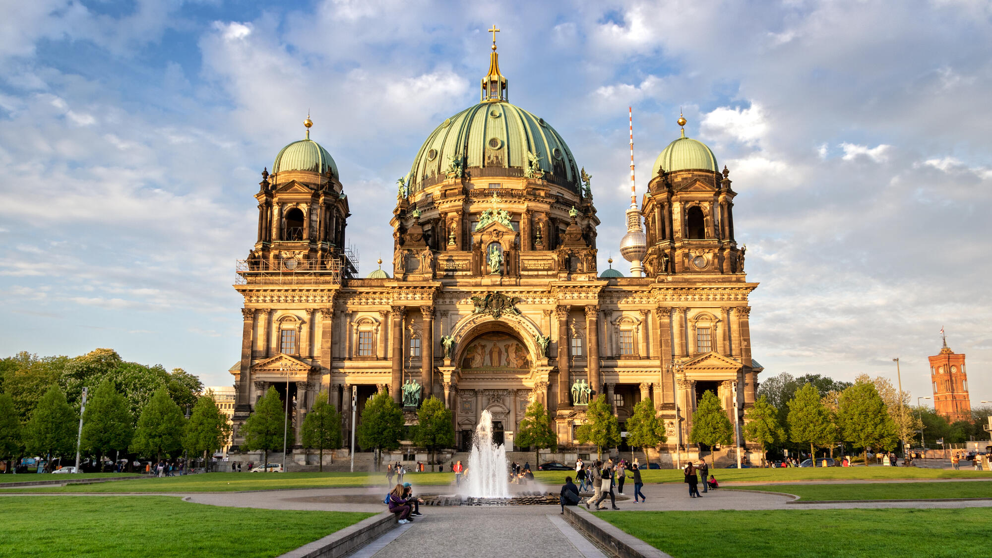 Berlin Cathedral behind the fountain and lawns of the Lustgarten beneath a partly cloudy sky.