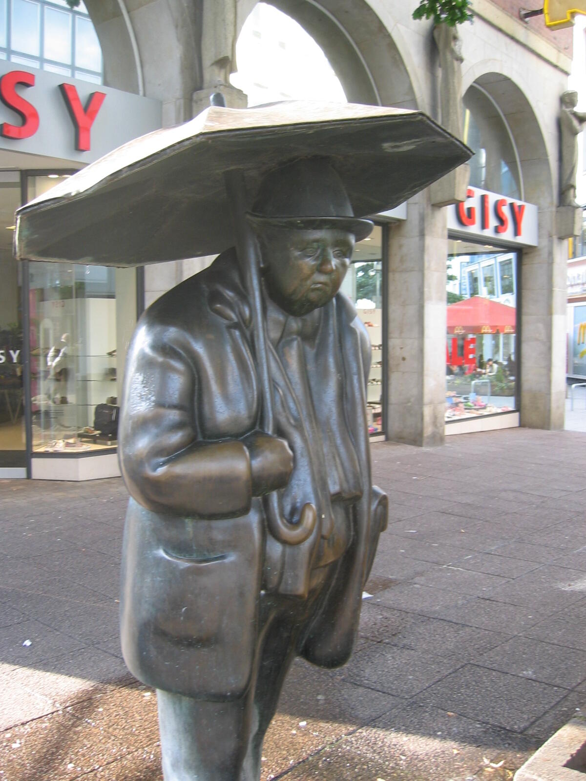 Bronze figure of a man with an umbrella outside a shop