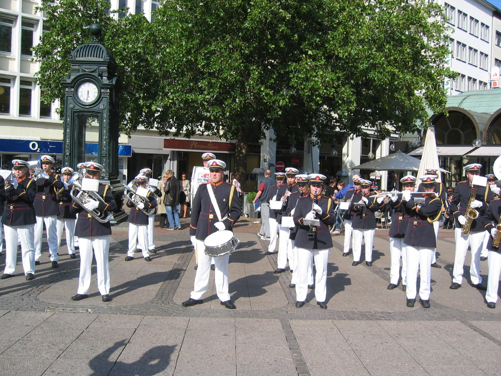 Uniformed marching band with wind instruments, with the Kröpcke Clock behind them