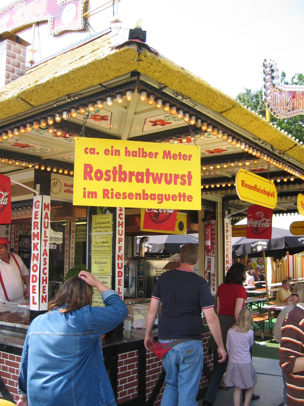 Snack stand with a sign reading “approx. half a metre of grilled sausage in a giant baguette”