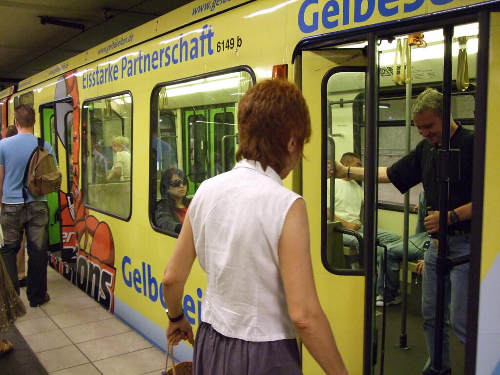Yellow-liveried light rail carriage with an open door as passengers board
