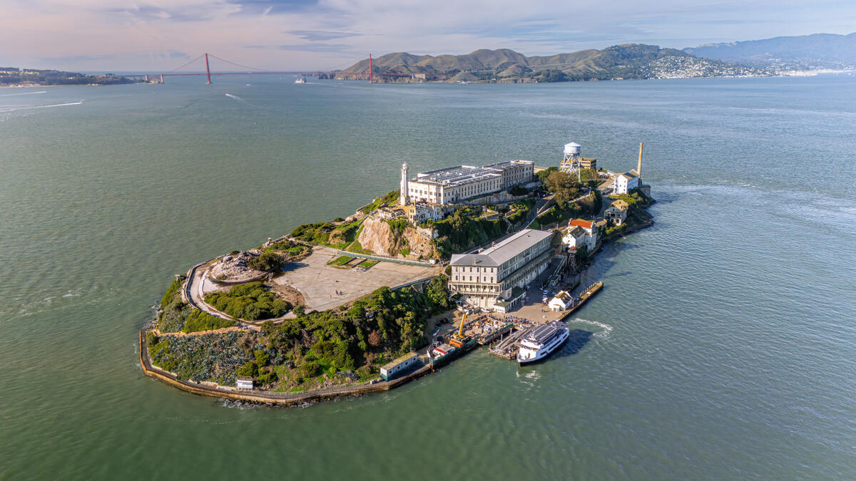 The island's prison buildings, paths and landing sit in the bay, with the Golden Gate Bridge visible on the horizon.