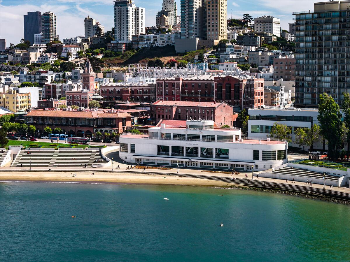 An elevated view of the curved bathhouse, seating terraces and narrow beach beneath the densely built hillside.