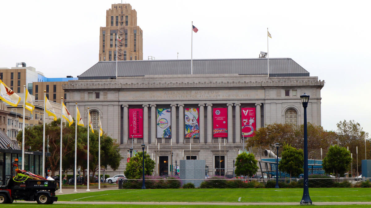 The stone museum building, with tall columns, flags and exhibition banners, stands beyond a lawn.
