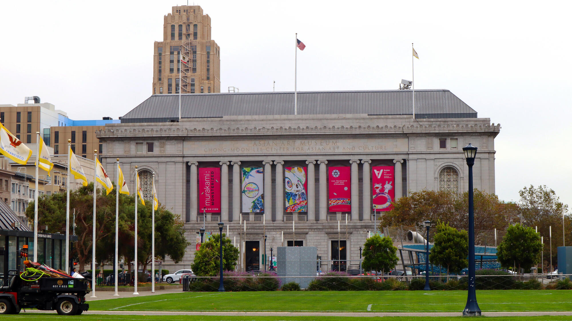 The stone museum building, with tall columns, flags and exhibition banners, stands beyond a lawn.