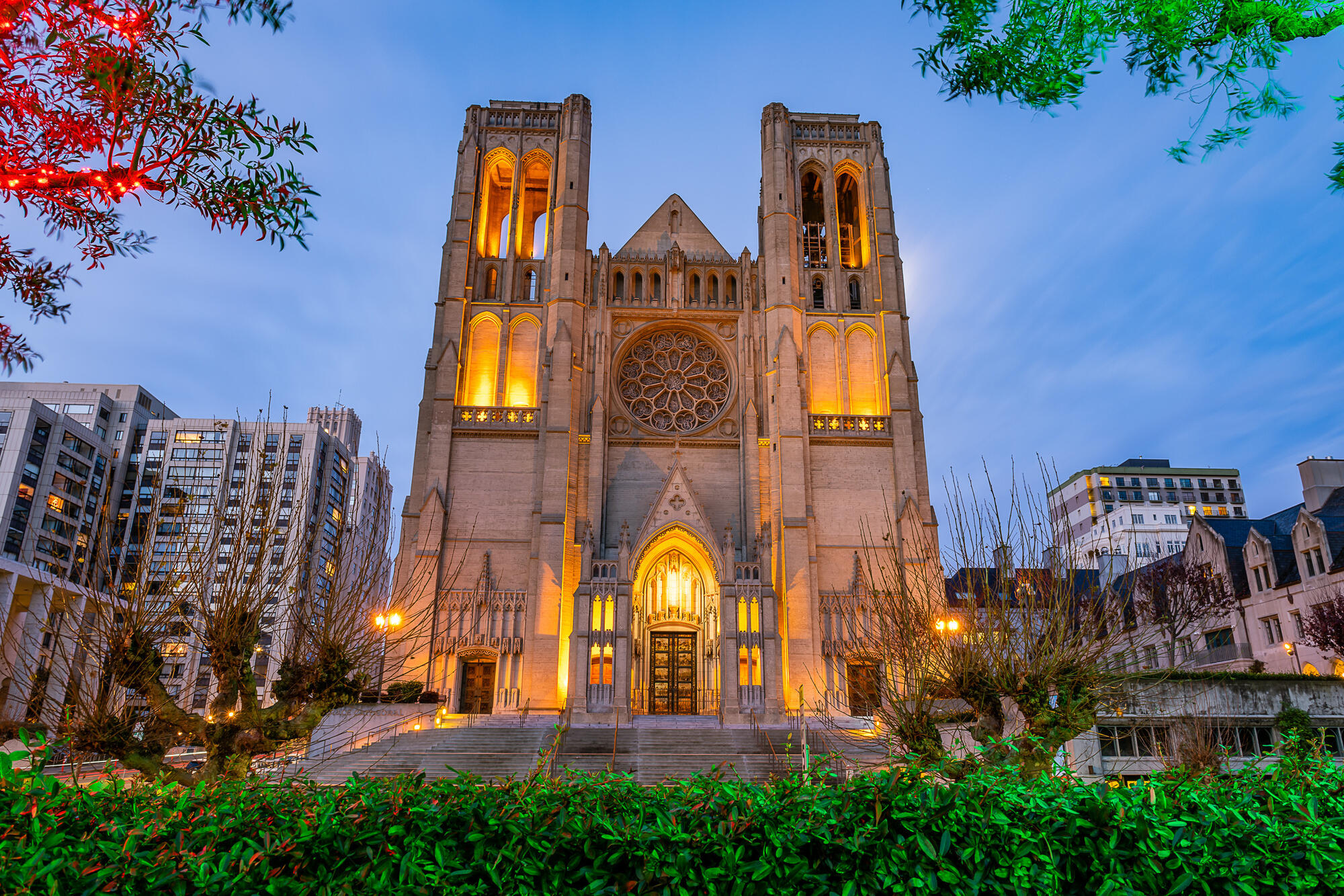 Warm light picks out Grace Cathedral's bell openings, rose window and entrance at dusk.