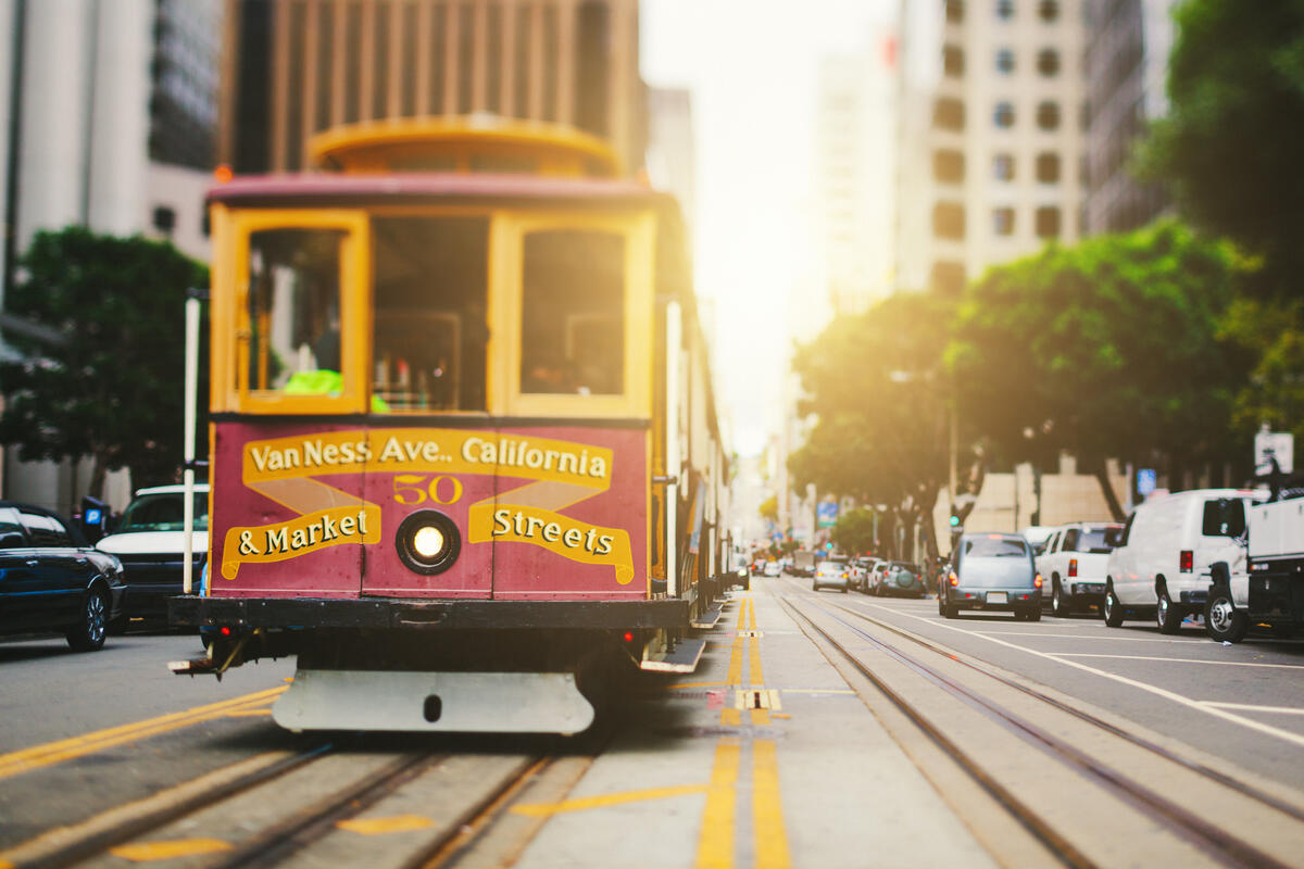 A red and yellow cable car passes between tall buildings in warm light on California Street.