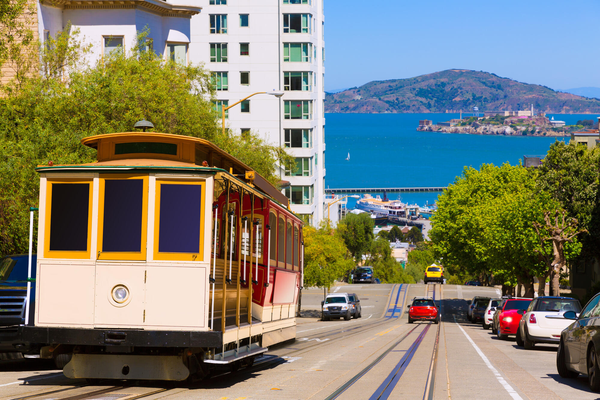 A cable car on steep Hyde Street, with a view of the bay between the buildings.