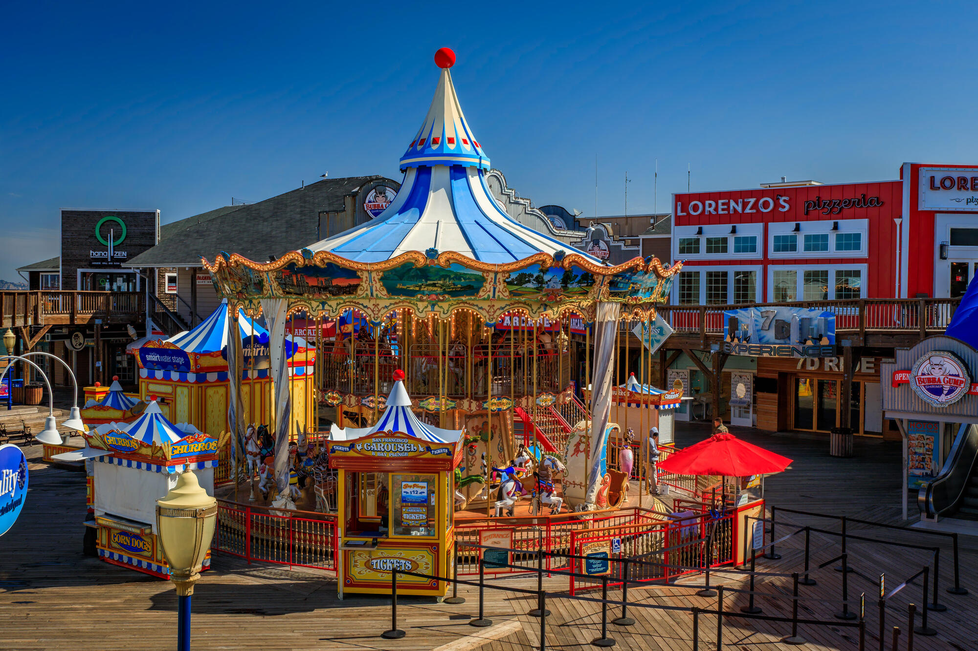 The two-level carousel, with its blue and white roof, gold-coloured poles and colourful horses, stands among the pier's shops.