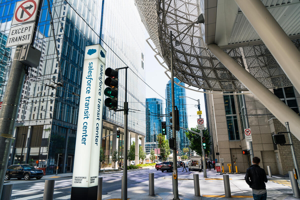 A sign column, glass surfaces and angled supports mark the entrance beneath the overhanging building.