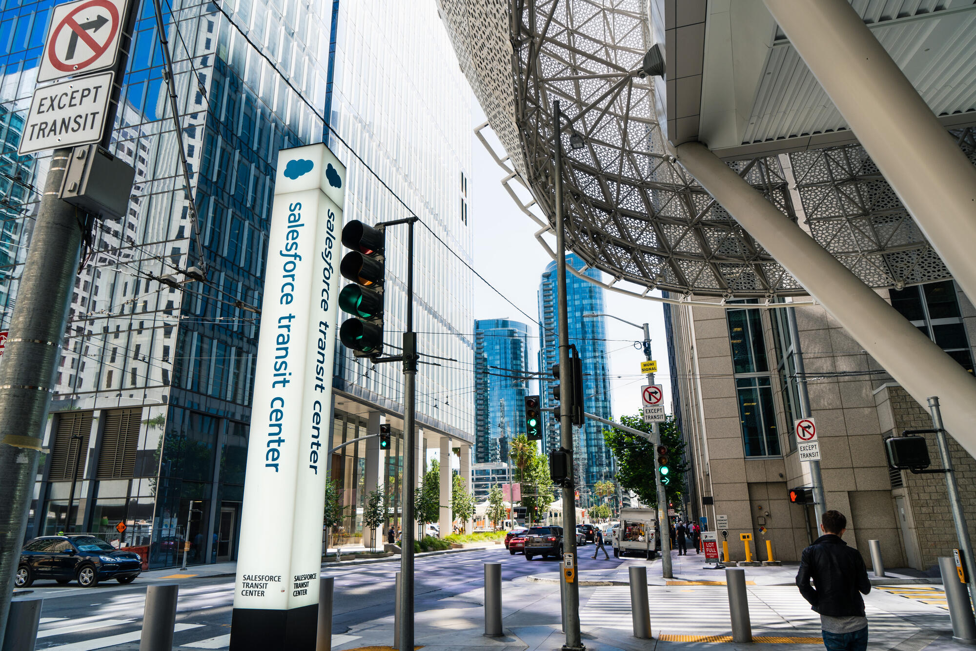 A sign column, glass surfaces and angled supports mark the entrance beneath the overhanging building.