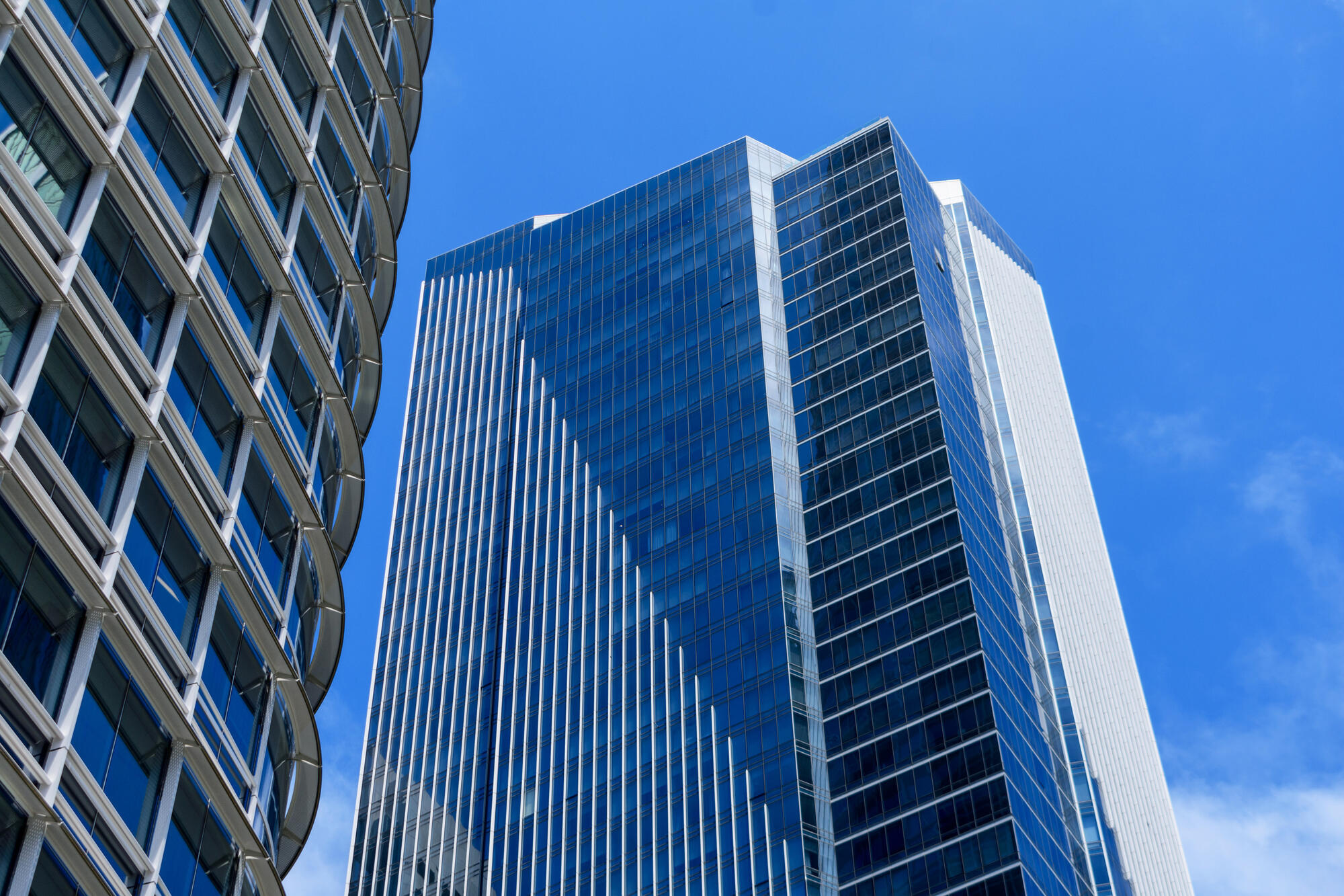 An upward view of blue glazing, pale vertical facade strips and the curved edge of Salesforce Tower.