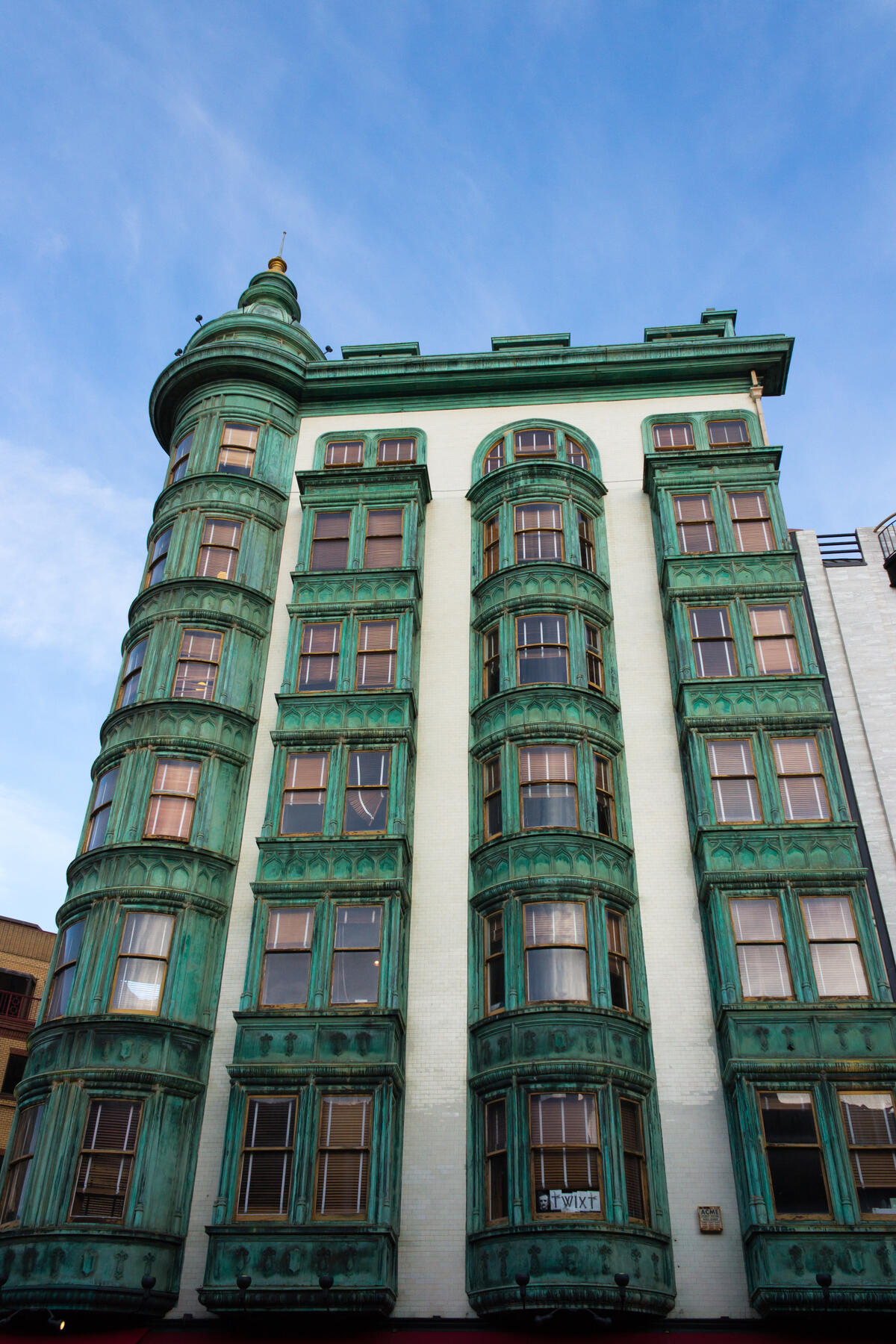 An upward view of the Sentinel Building's green facade, projecting bay windows and rounded corner turret.