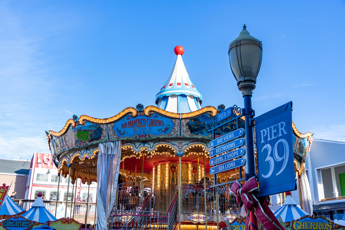 The carousel's blue and white roof and gold-coloured decoration stand beside Pier 39's direction signs.