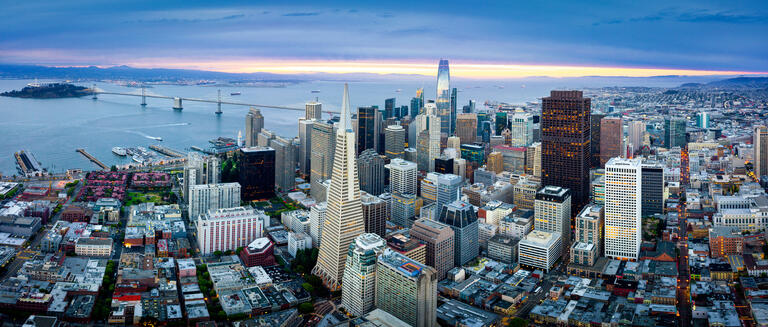 An aerial view across downtown's closely packed towers and streets towards the bay.