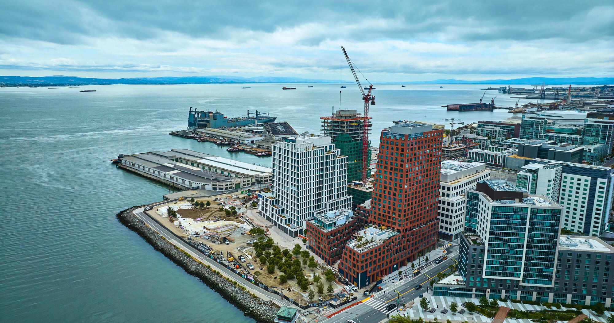 An aerial view of Mission Rock's waterfront, with new glass buildings, a high-rise under construction and a crane.