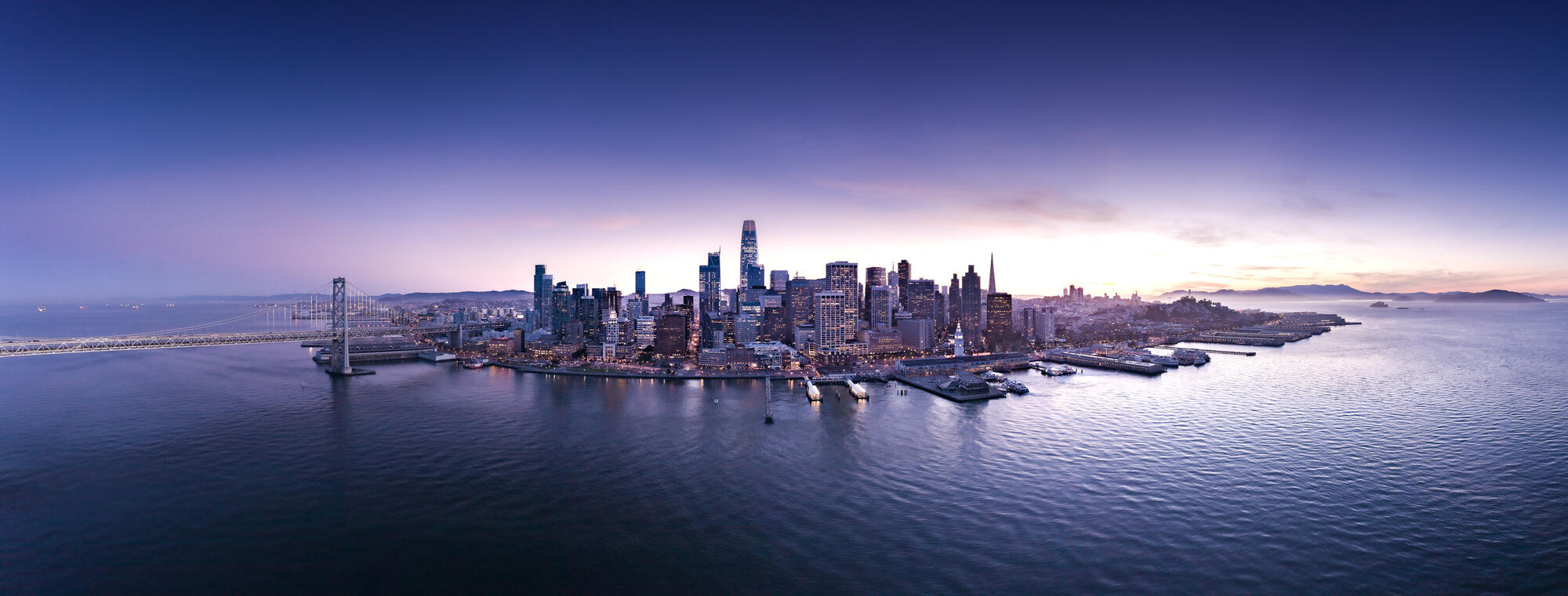 Downtown and its piers stand against the broad expanse of the bay at dusk.