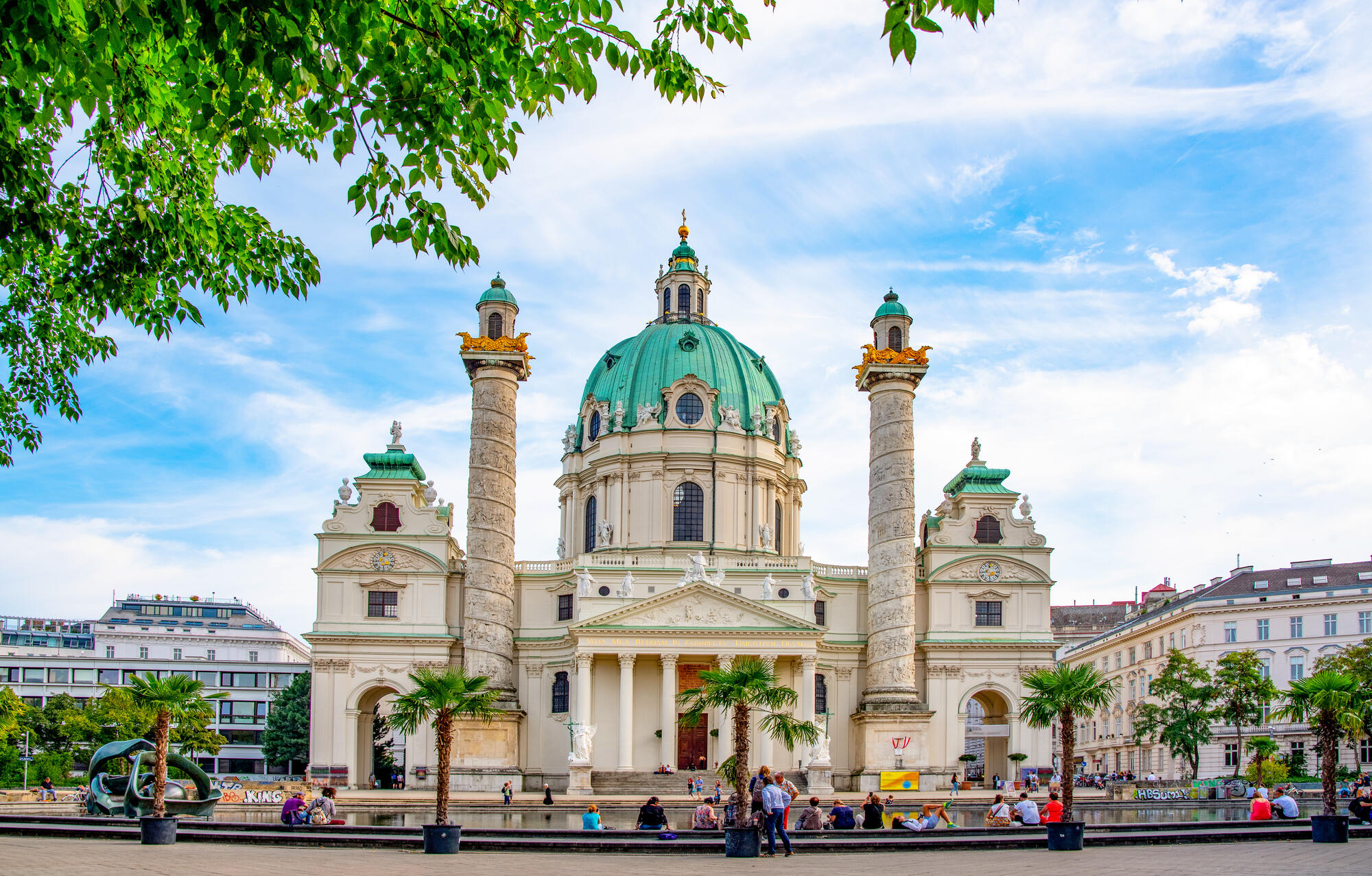 Karlskirche with its dome and columns on Karlsplatz in Vienna; people sit beside the pool in front.